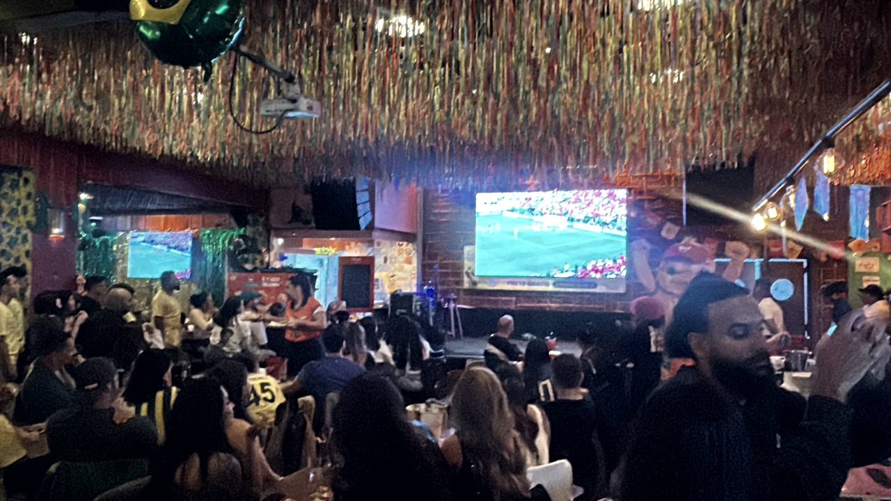 Casa cheia durante a transmissão de um jogo, com o telão ao fundo
